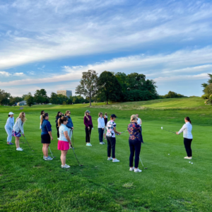 Group of ladies learning golf during a Birdies and Bubbly class at Reston National Golf Course, standing on the first fairway with clubs in hand. 
