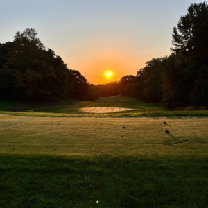 Sunrise over a tee box at Reston National Golf Course, casting warm light on the fairway and creating a serene morning golf scene.